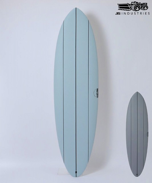 Tall light-blue surfboard displayed upright on a stand, with a smaller gray board next to it on a white wall (JS Industries logo in corner).