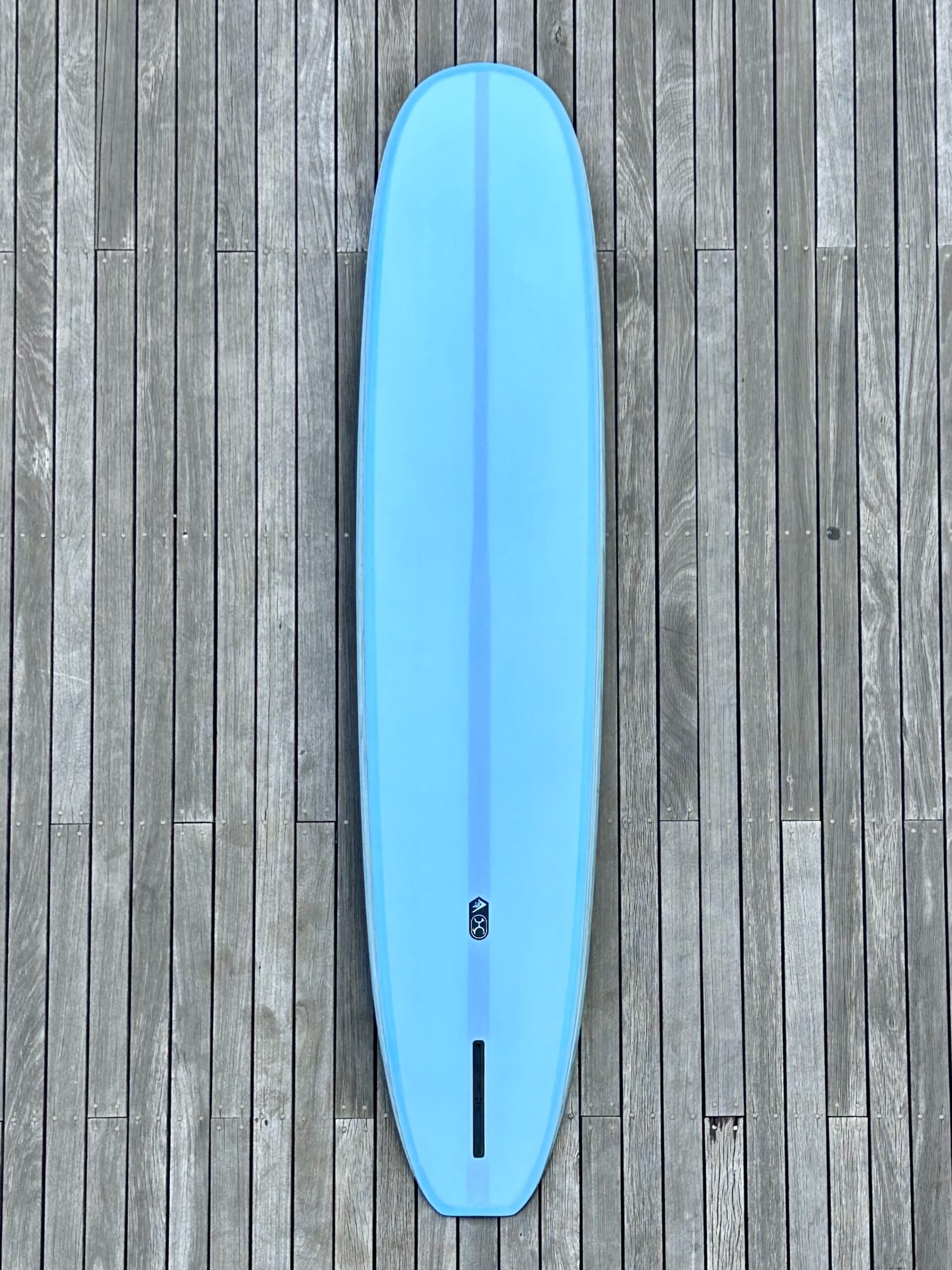 IMG_2621 - SHOP NEWS | ムラサキスポーツオンラインストア 通販 Top-down view of a bright blue surfboard resting on a weathered wooden dock surface.