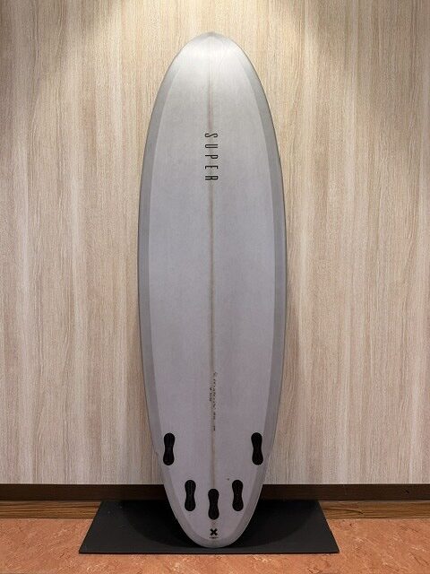 White surfboard standing upright against a wall, resting on a black display mat indoors.