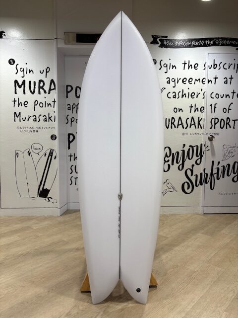 White surfboard standing upright on a wooden stand inside a shop, with bold black handwriting murals on the walls around it.