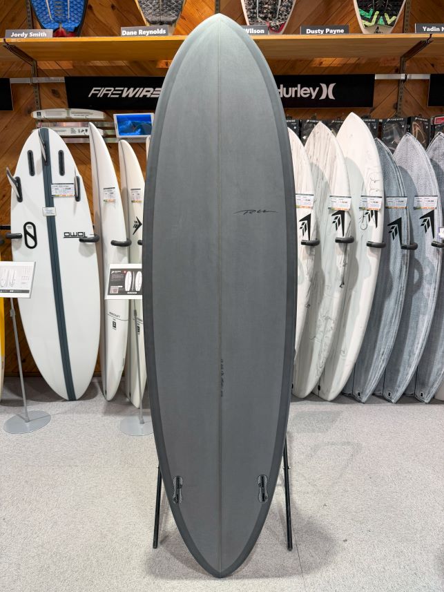 Gray surfboard on a stand in a surf shop, with a row of boards on shelves behind it.