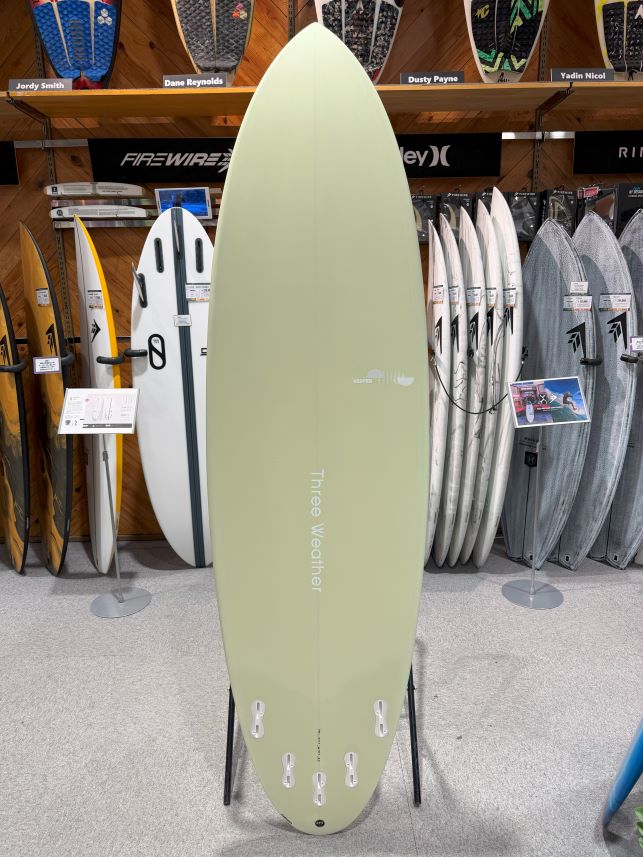 Pale green surfboard on a stand inside a surf shop, with racks of boards in the background.