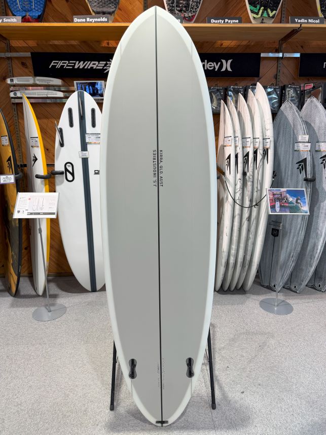 Light gray surfboard on a stand in a surf shop, with other boards displayed on racks in the background.