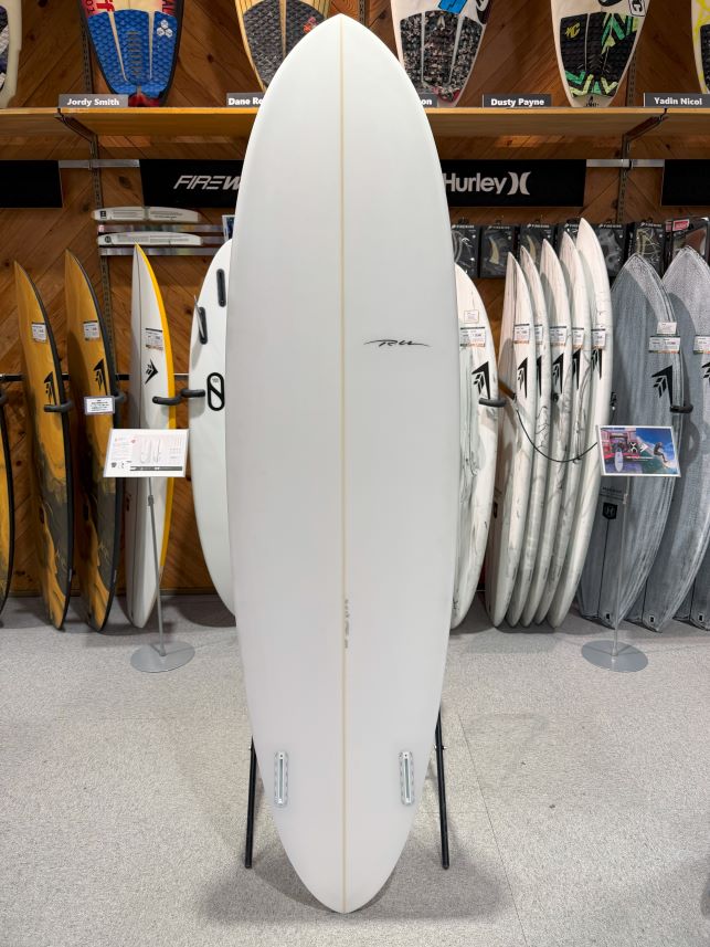 White surfboard on a stand in a surf shop, with other boards on racks in the background.
