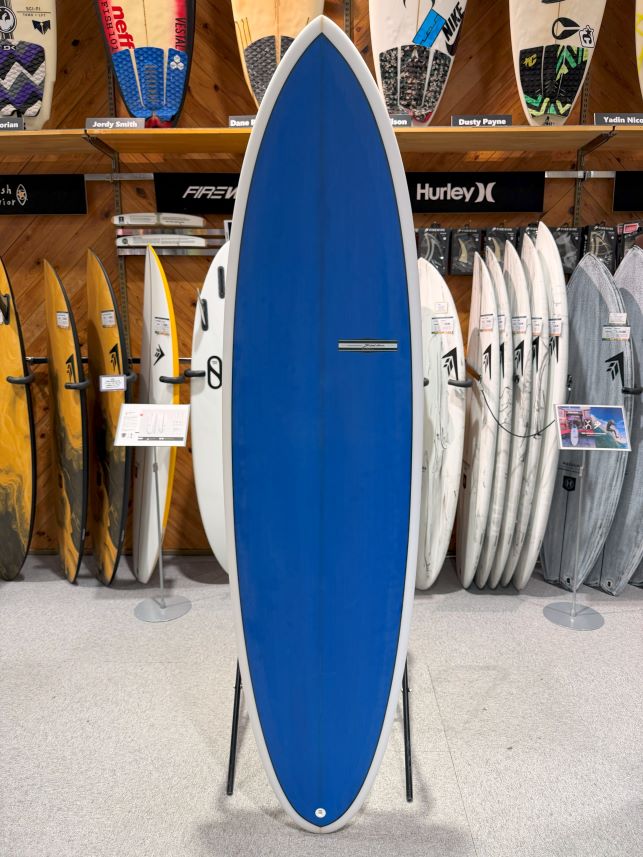 Blue surfboard on a stand in a surf shop display, with other boards lined up behind it on racks.