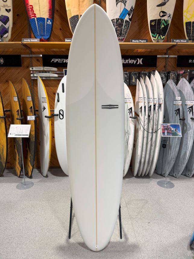White surfboard on a stand in a surf shop, surrounded by other boards on racks and shelves.