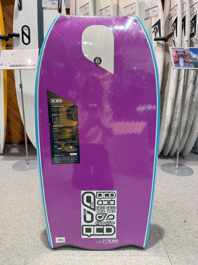 Purple stand-up paddleboard on display in a store, with blue edge trim and sticker panels on the front.