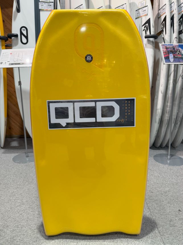 Yellow rescue board or bodyboard with a large QCD sticker in front, stored in a showroom with other boards in the background