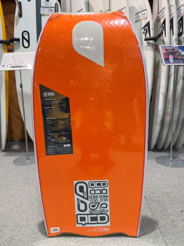 Orange windsurfing board on display in a shop, with other boards in the background.