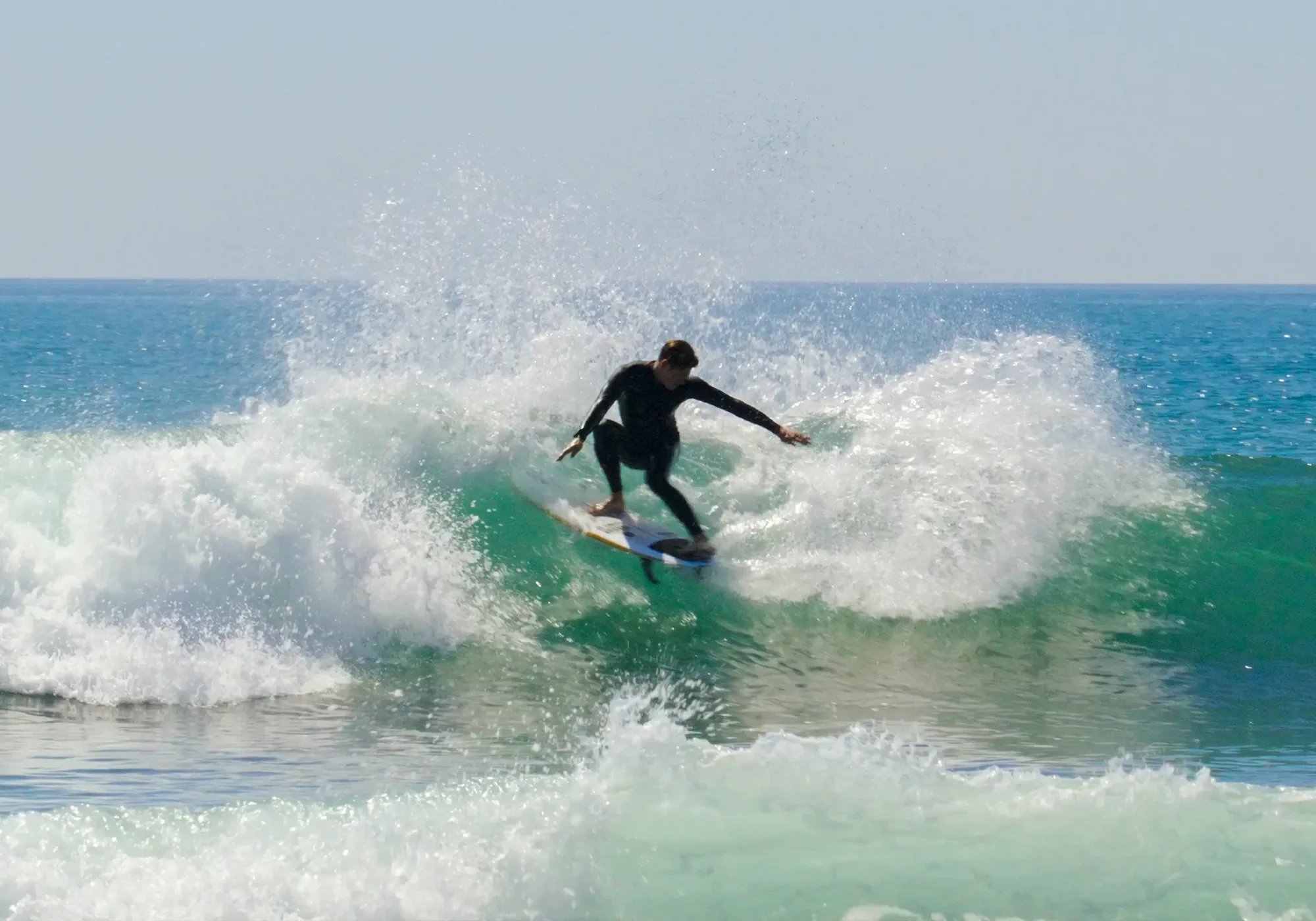 Surfer in a wetsuit carving a wave with water spraying around them near the shore.