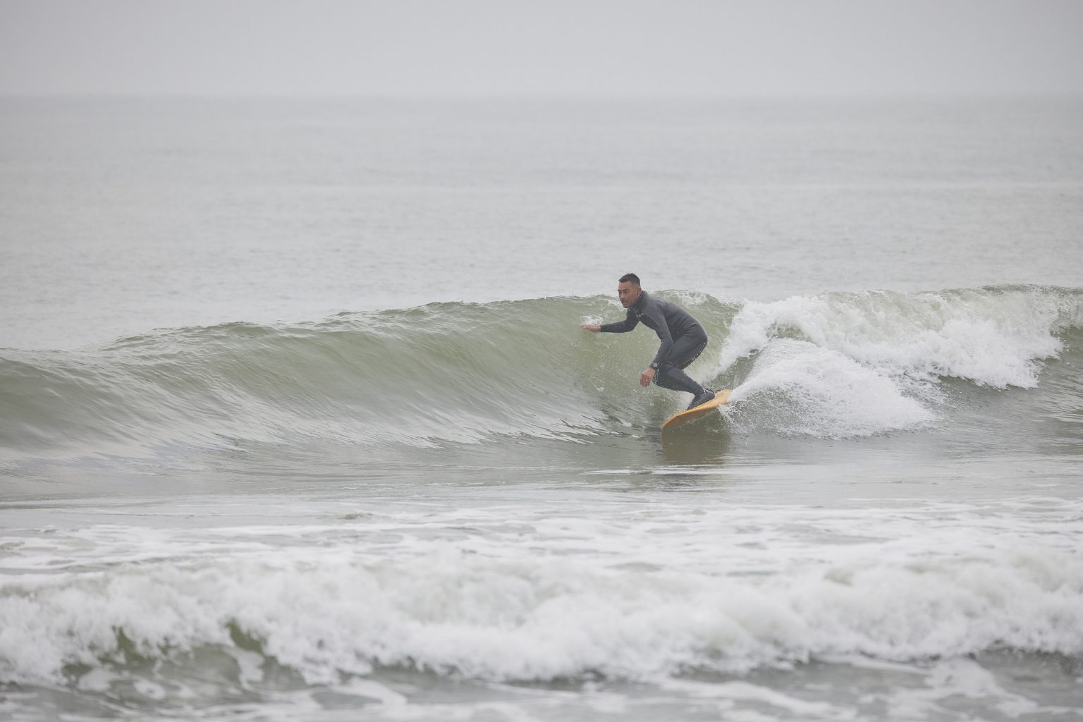 Surfer in a black wetsuit rides a green-tinted wave on a yellow board.