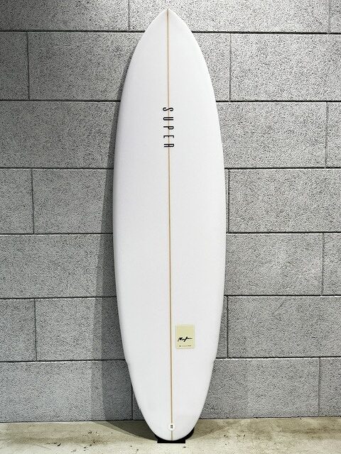 s-IMG_3502 - SHOP NEWS | ムラサキスポーツオンラインストア 通販 White surfboard with a narrow yellow stringer leaning against a gray brick wall.