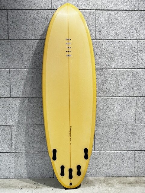 s-IMG_3505 - SHOP NEWS | ムラサキスポーツオンラインストア 通販 Yellow surfboard with multiple black fins leaning against a gray brick wall.