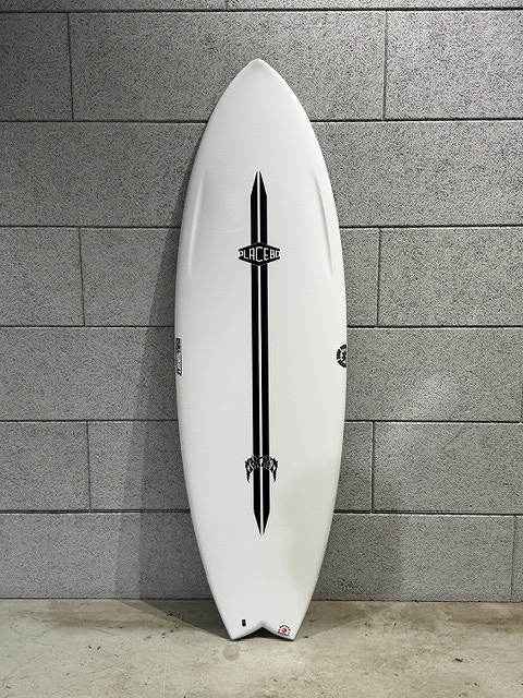 White surfboard with a bold black vertical stripe and logos, standing upright against a gray cinder block wall for scale and context.