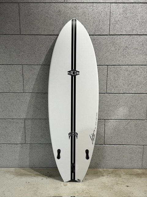 White surfboard with a bold black center stripe, leaning upright against a gray tiled wall.