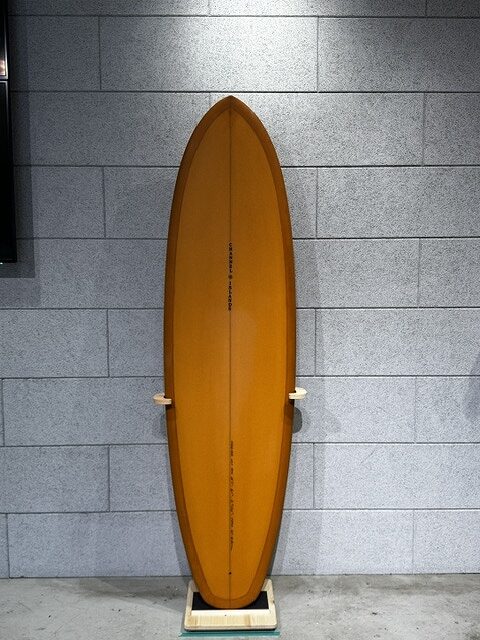 Orange surfboard standing upright on a wooden rack against a gray tiled wall indoors.