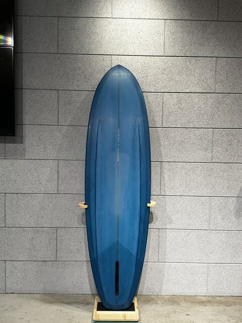 Blue surfboard standing upright on a wooden stand against a gray tiled wall.