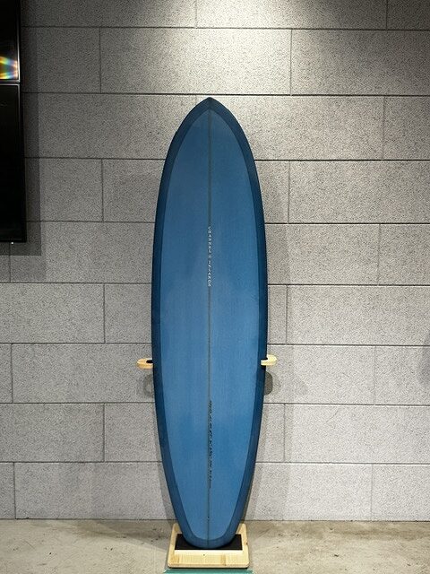 Blue surfboard standing upright on a wooden display rack against a gray tiled wall indoors