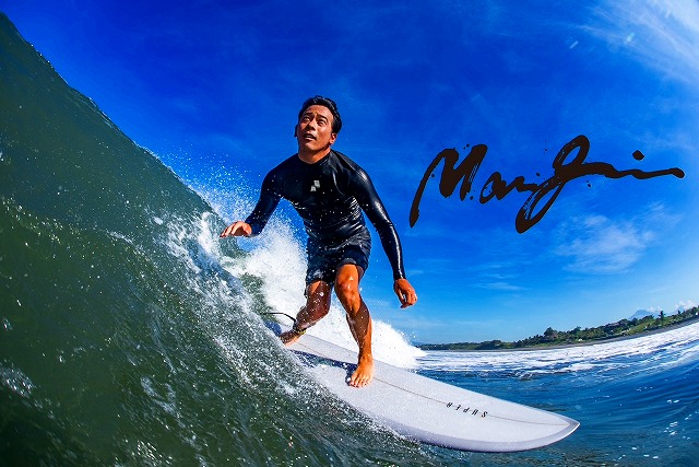 マージン 00 - SHOP NEWS | ムラサキスポーツオンラインストア 通販 Surfer in a black wetsuit rides a cresting wave on a white surfboard under a bright blue sky.