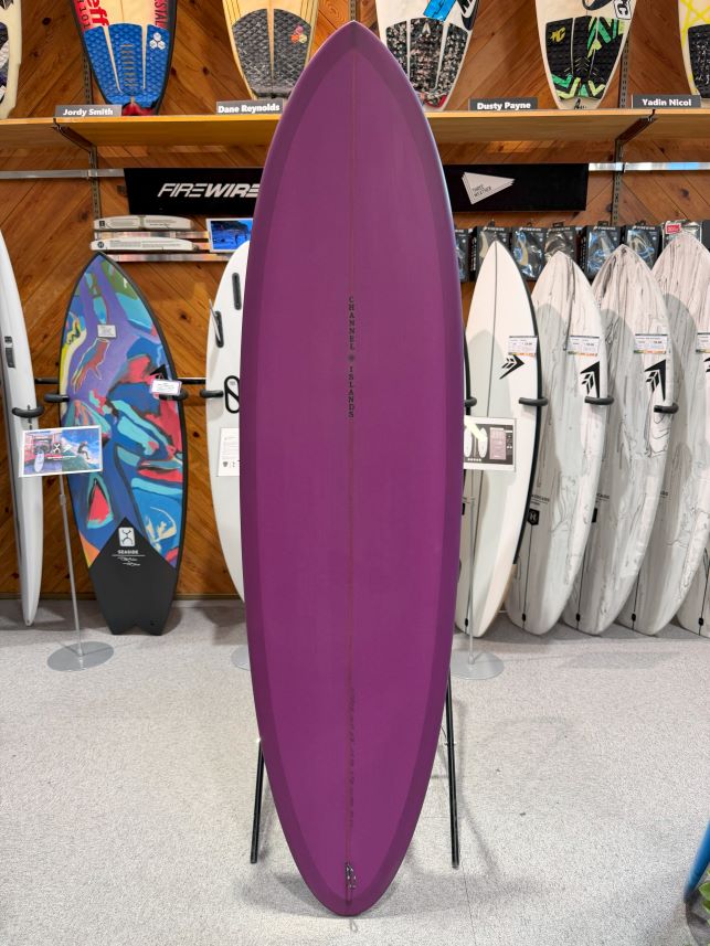 IMG_0225 - SHOP NEWS | ムラサキスポーツオンラインストア 通販 Purple surfboard standing upright on a display stand inside a surf shop, with other boards lined up behind it.