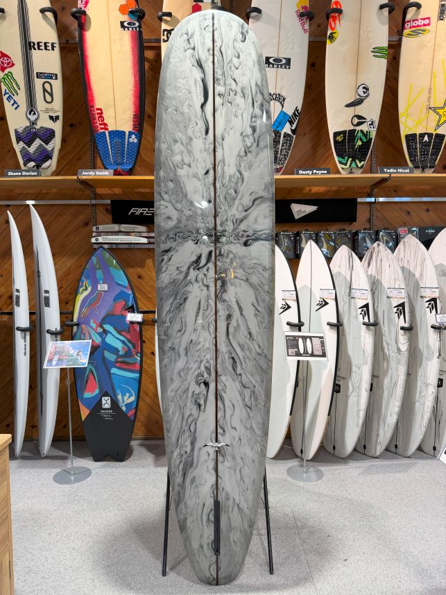 Marble-gray longboard on a stand in a surf shop, surrounded by other boards on display.