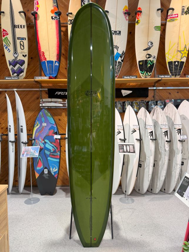 Green surfboard on a stand in a shop, surrounded by other boards on racks outside and on the wall display.