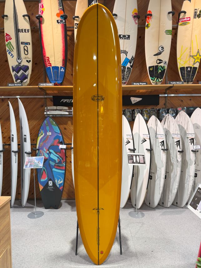 Yellow surfboard on a stand in a shop, surrounded by other boards on racks.